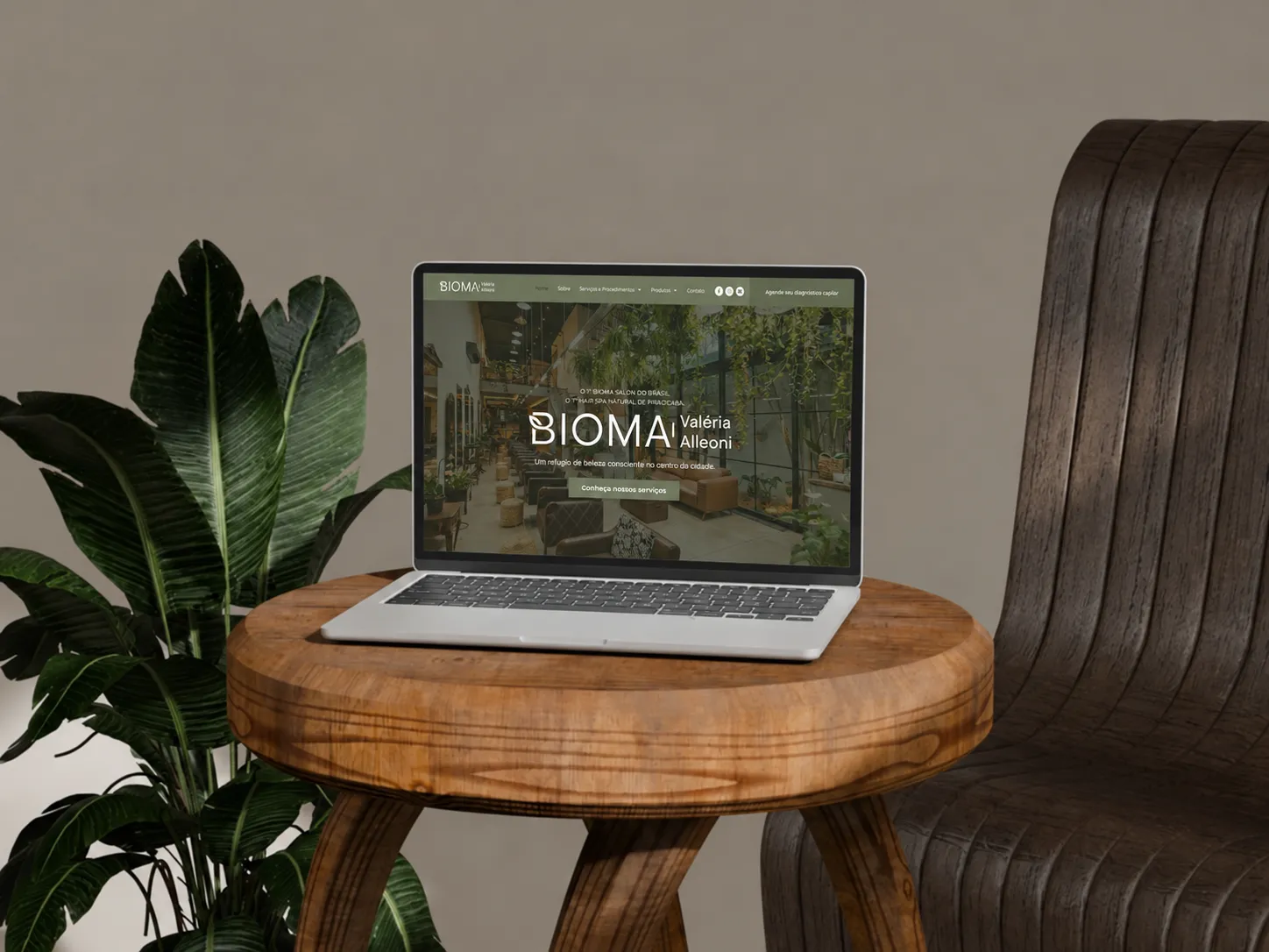 Notebook sobre banqueta de madeira exibindo o site do Bioma Salon Valéria Alleoni, ao lado de uma planta